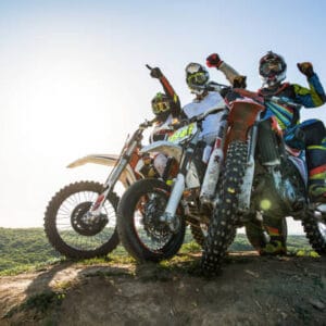 Low angle view of three motocross riders on stunt bikes on top of hill with hands raised.