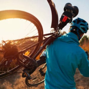 Rear view of a mountain biker carrying a bicycle on his shoulder over the nature trail.