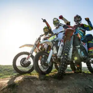 Low angle view of three motocross riders on stunt bikes on top of hill with hands raised.