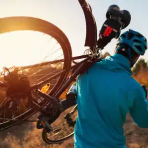 Rear view of a mountain biker carrying a bicycle on his shoulder over the nature trail.